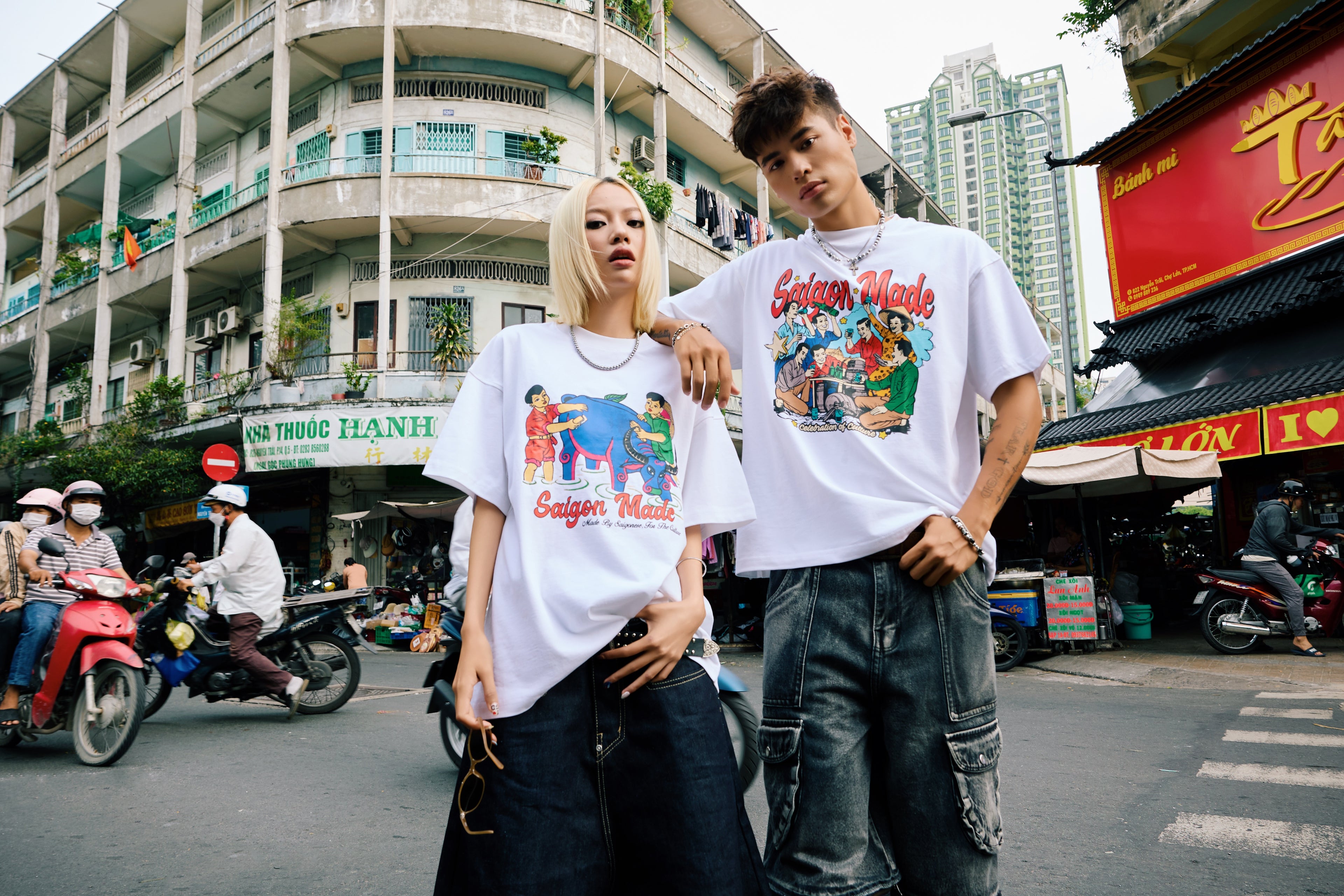 Two people wearing matching white t-shirts with colorful graphics on a street.
