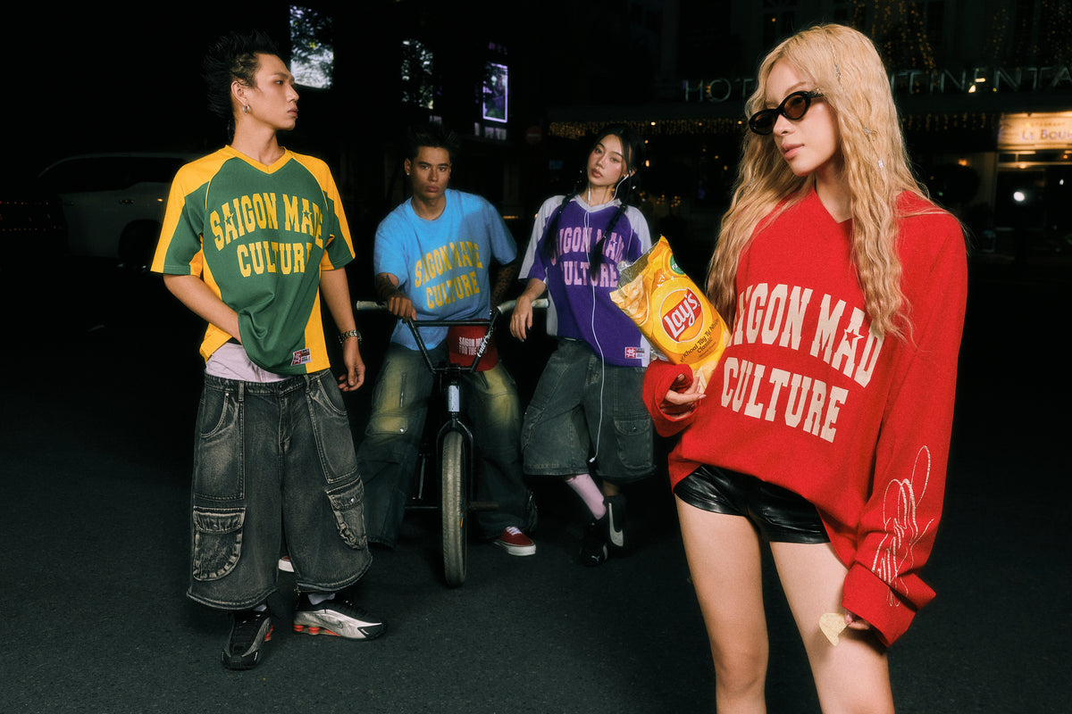 Four young people in streetwear apparel posing at night on a city street. One model in the foreground wears an oversized red sweatshirt with 'SAISON MAD CULTURE' text, holding a bag of Lay's chips.