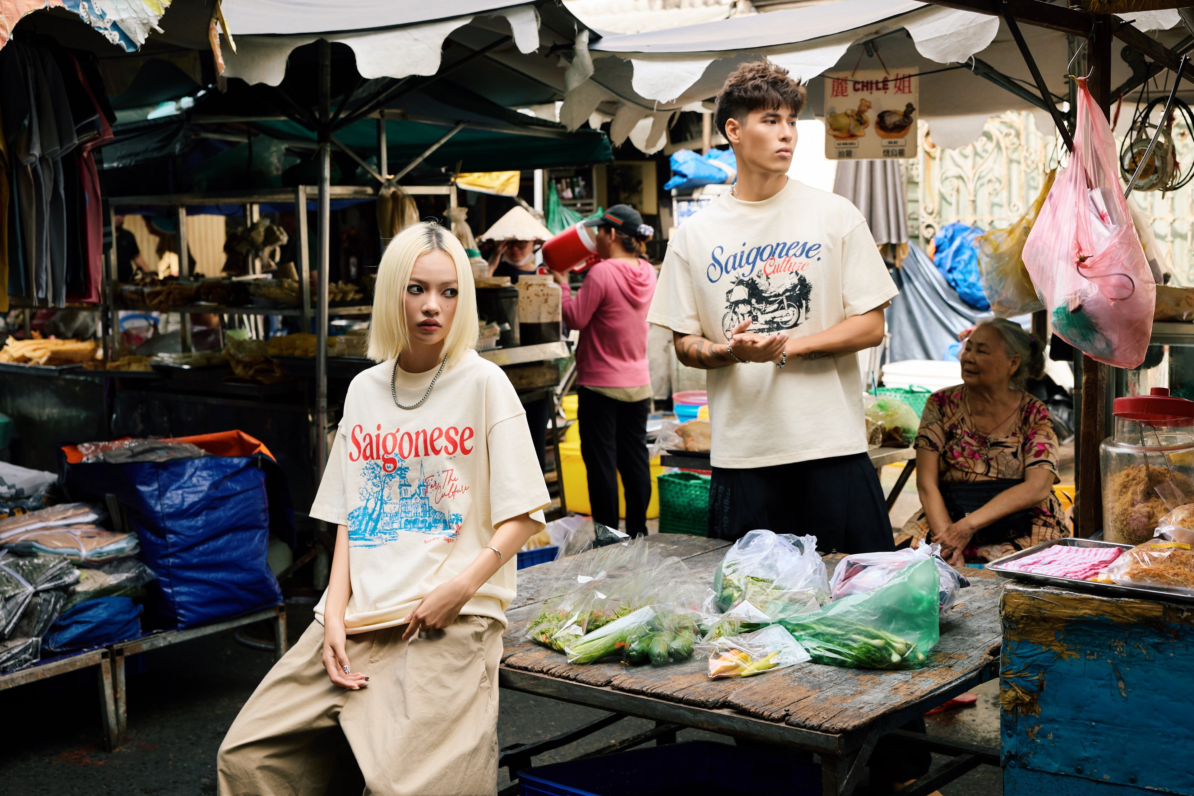 Two people in a market setting wearing 'Saignese' t-shirts.